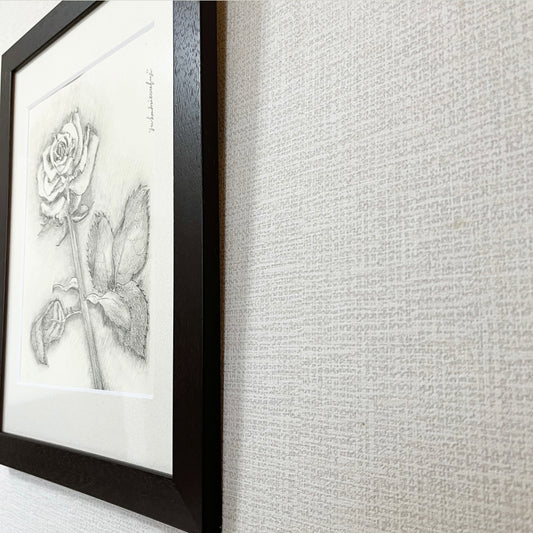A framed pencil drawing of a fresh and beautiful rose, viewed from a slight angle, highlighting the texture and depth of the artwork.  みずみずしいバラの鉛筆画を額装し、斜めから撮影した画像。作品の質感や奥行きを際立たせています。 已裝框鮮活玫瑰鉛筆畫的斜角視圖，突顯作品的質感與深度。